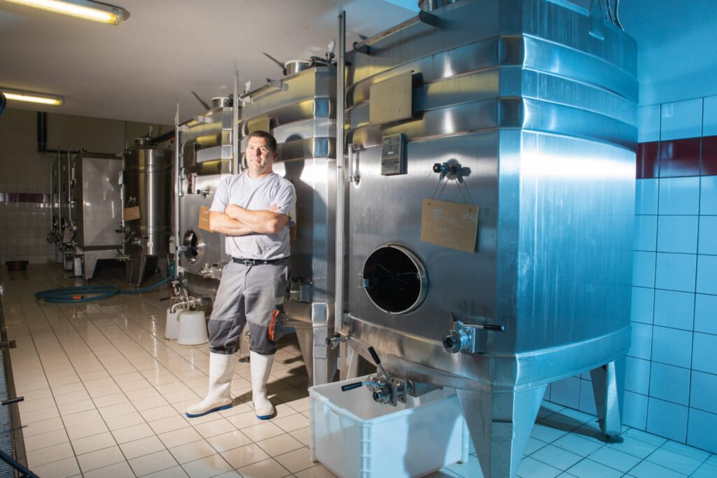 Vigneron posant devant des cuves en inox dans sa cave.